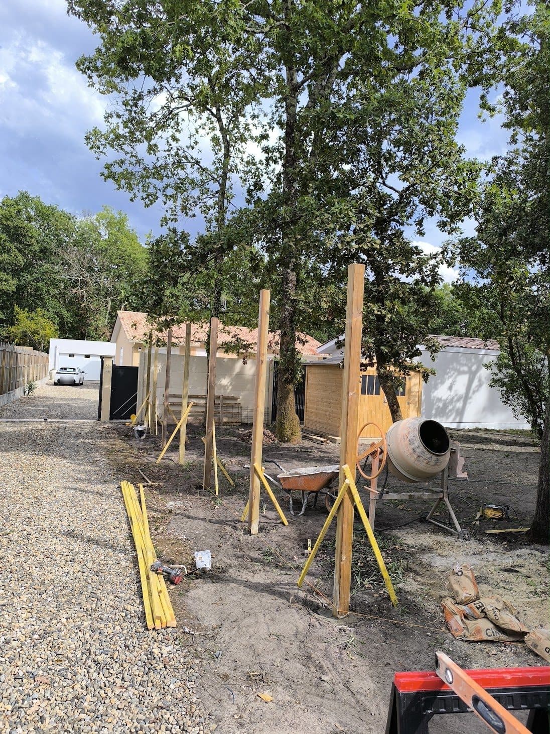 Poteaux bois scellés au béton et maintenus par des liteaux, bétonnière sur le chantier de clôture à Gujan-Mestras