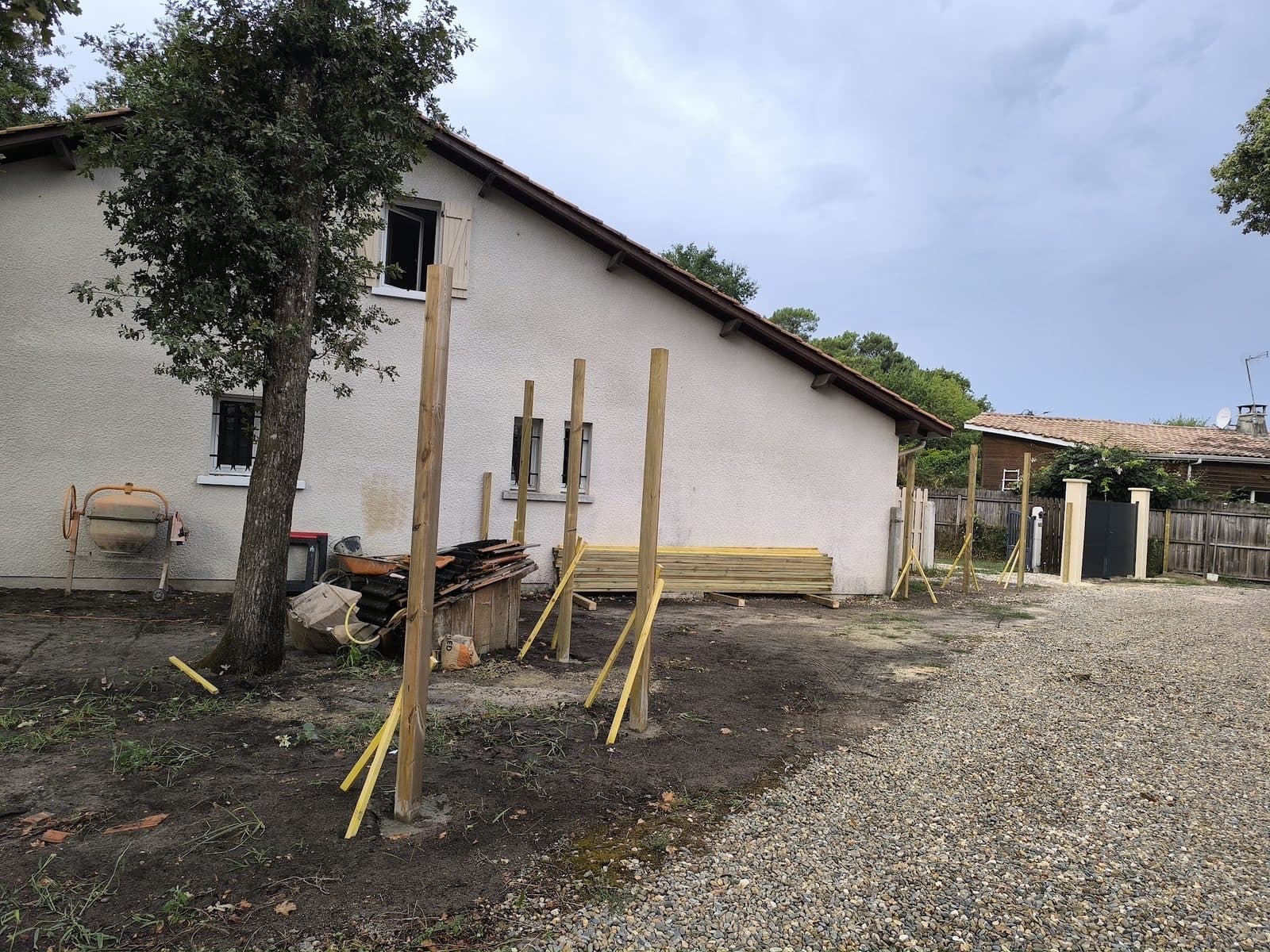 Poteaux bois tenus par des liteaux pendant la prise du béton, lames stockées contre la maison